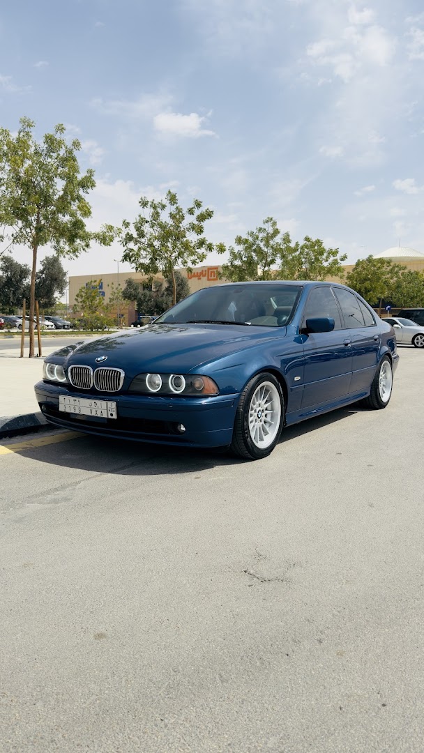 A blue BMW sedan parked outdoors with trees and a building in the background.