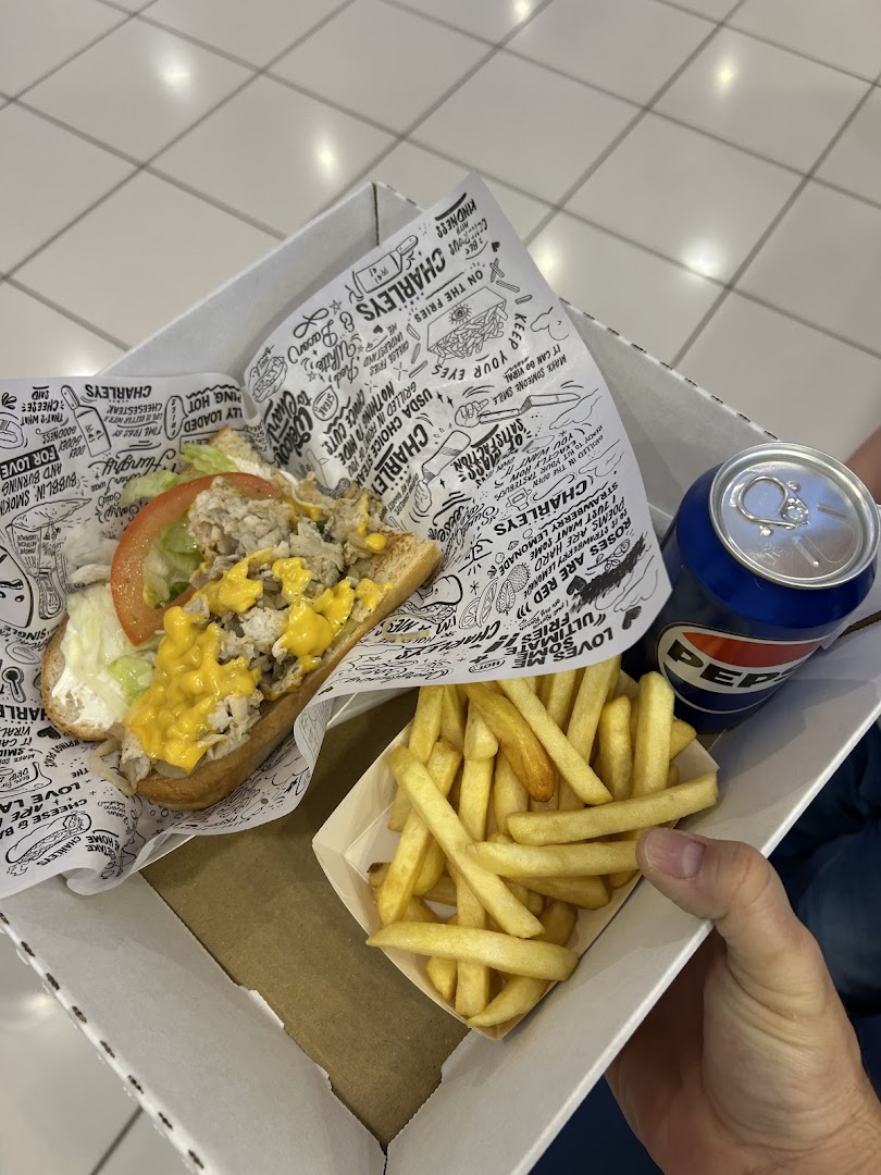 A hand holds a box containing a cheesesteak sandwich, french fries, and a can of Pepsi.