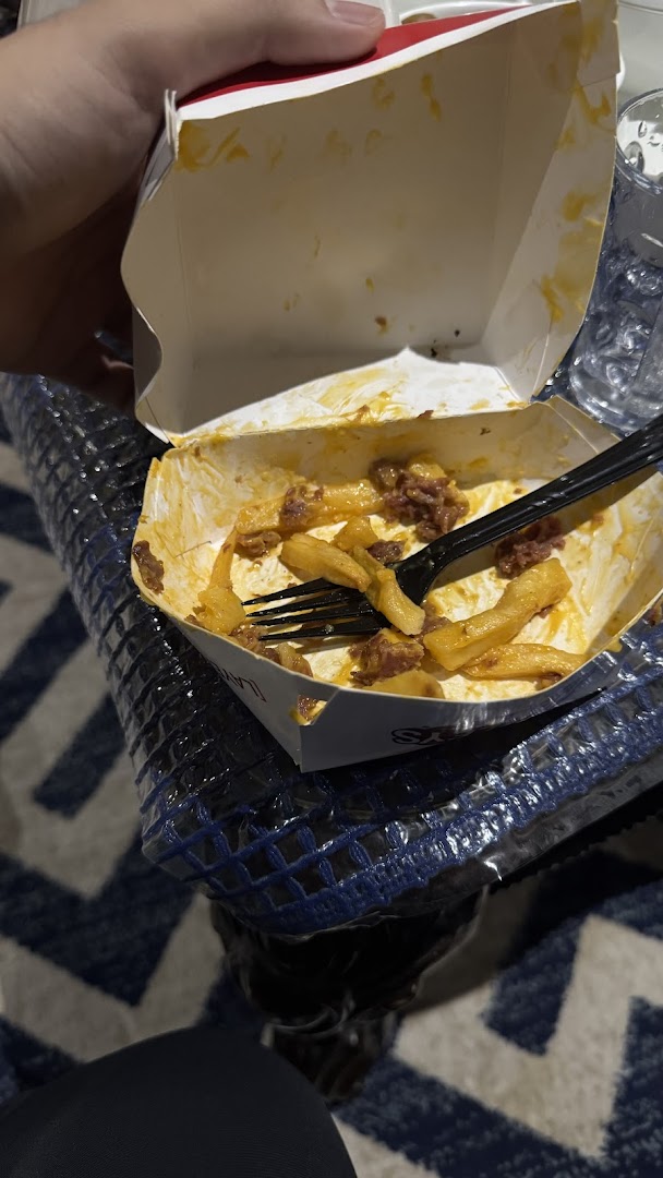 A partially eaten box of Charleys Cheesesteaks fries with cheese and meat.