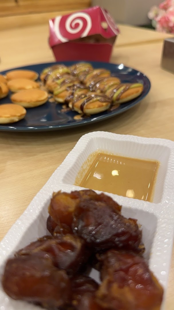 A close-up of dates with a dipping sauce and mini pancakes drizzled with chocolate.