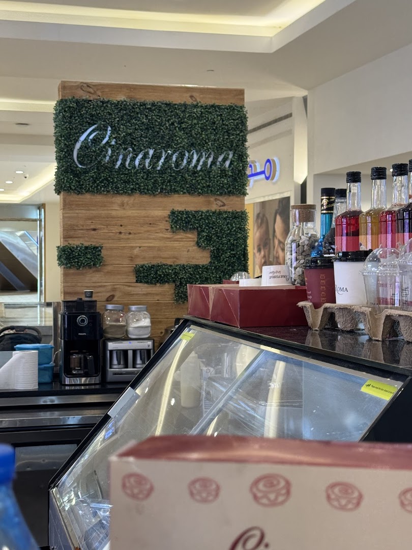 A Cinaroma coffee shop counter with coffee machines, syrups, and display cases.