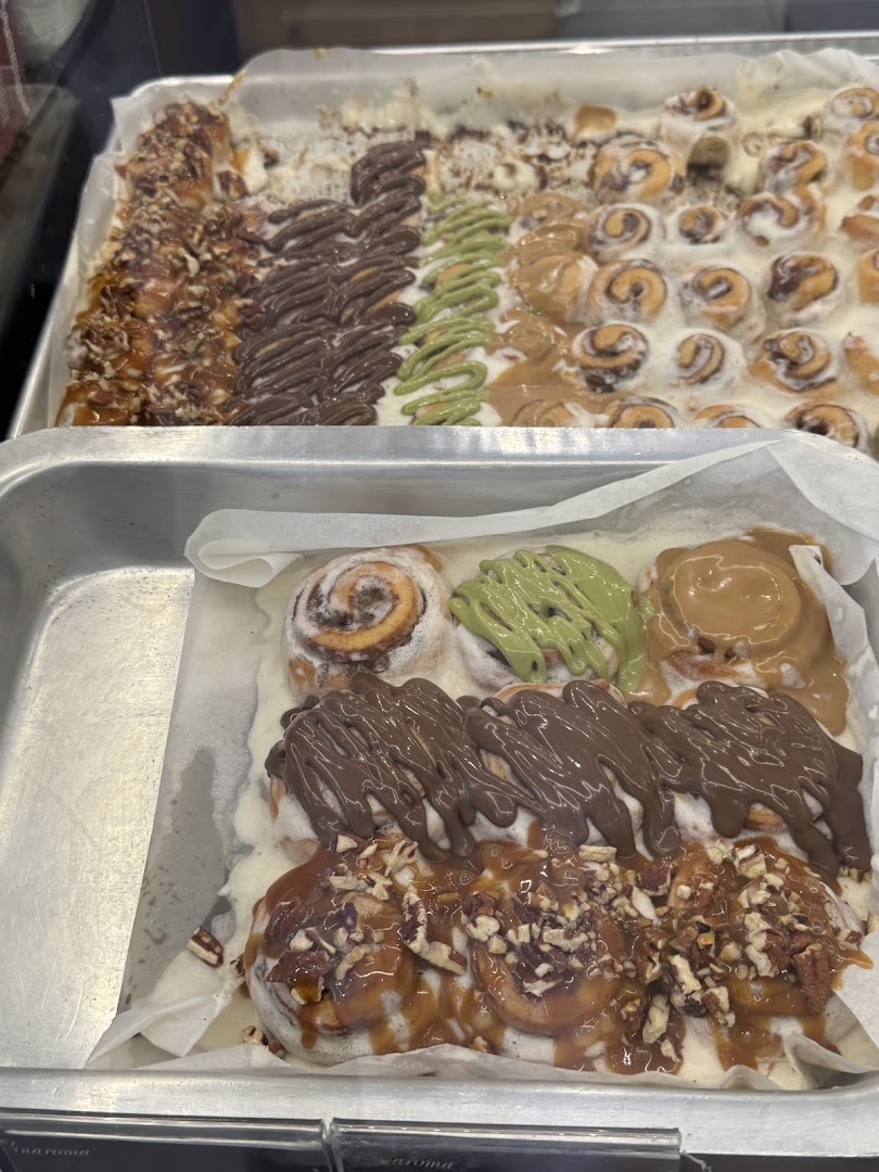 A close-up view of trays filled with delicious cinnamon rolls topped with various glazes and nuts.