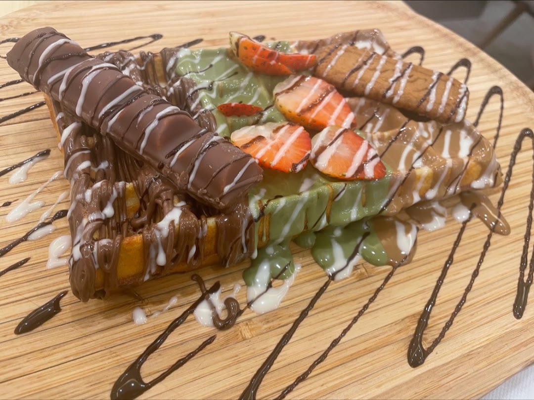 A delicious waffle topped with chocolate, strawberries, and biscuits on a wooden board.
