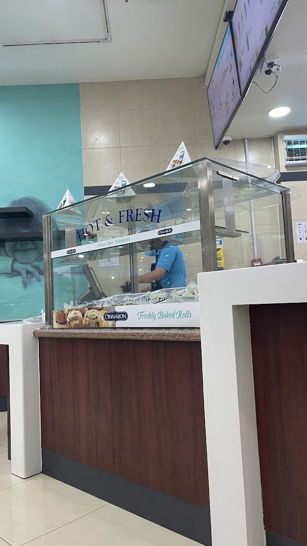A Cinnabon employee prepares orders behind a glass display case filled with cinnamon rolls.