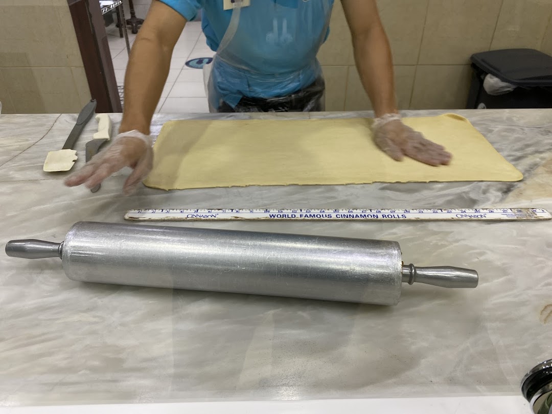 A baker is preparing dough for cinnamon rolls with a rolling pin and tools.