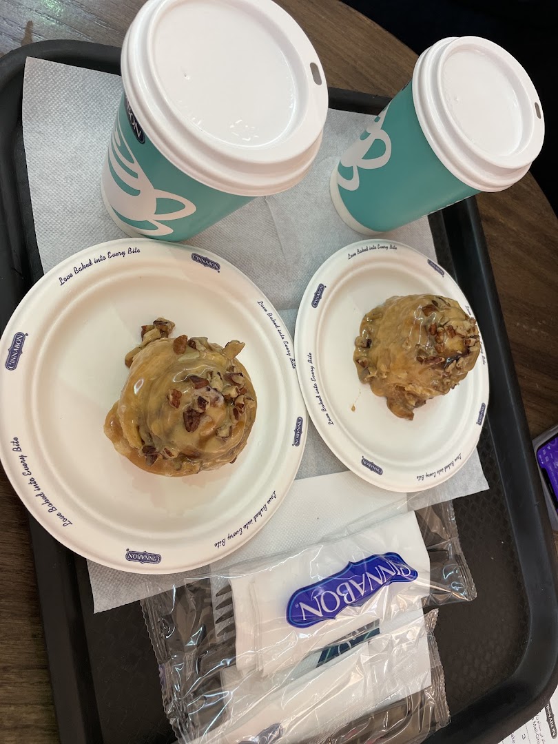 Two Cinnabon cinnamon rolls and drinks served on a tray with Cinnabon branded plates and napkins.