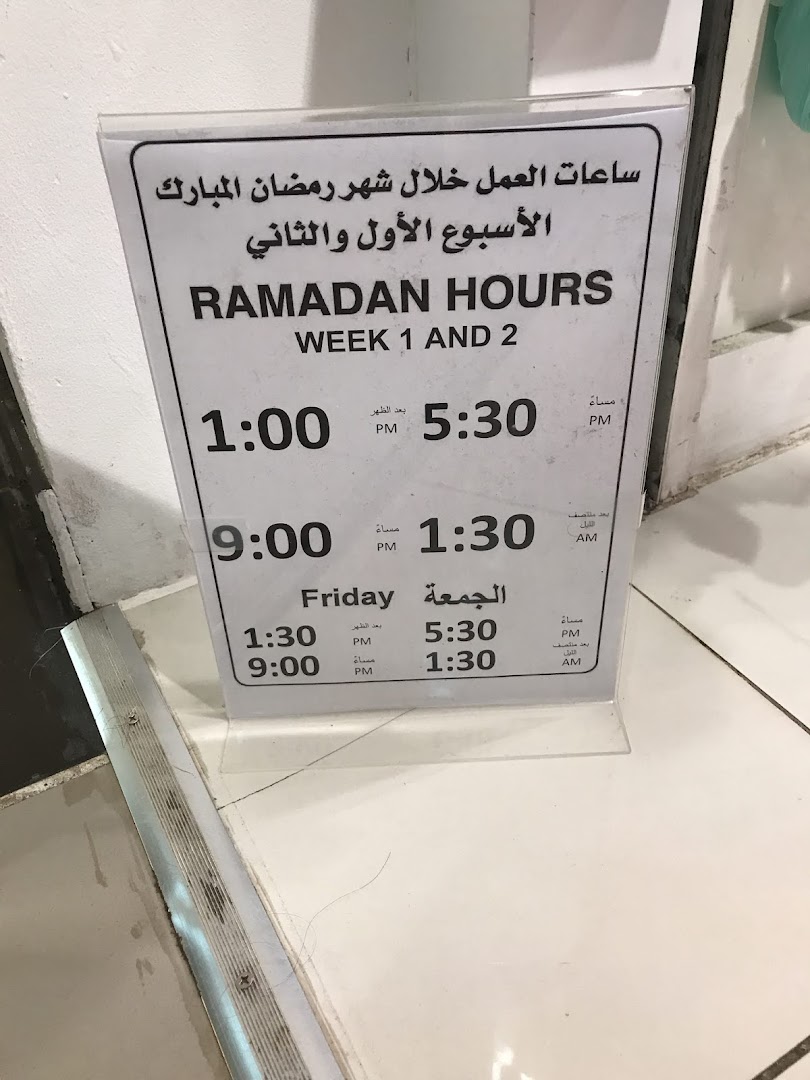 A sign displaying Ramadan working hours for Week 1 and 2, with times listed in Arabic and English.
