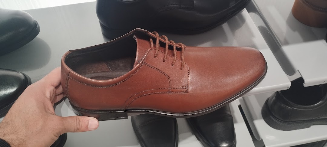A hand holds a brown leather dress shoe, showcasing its classic design.