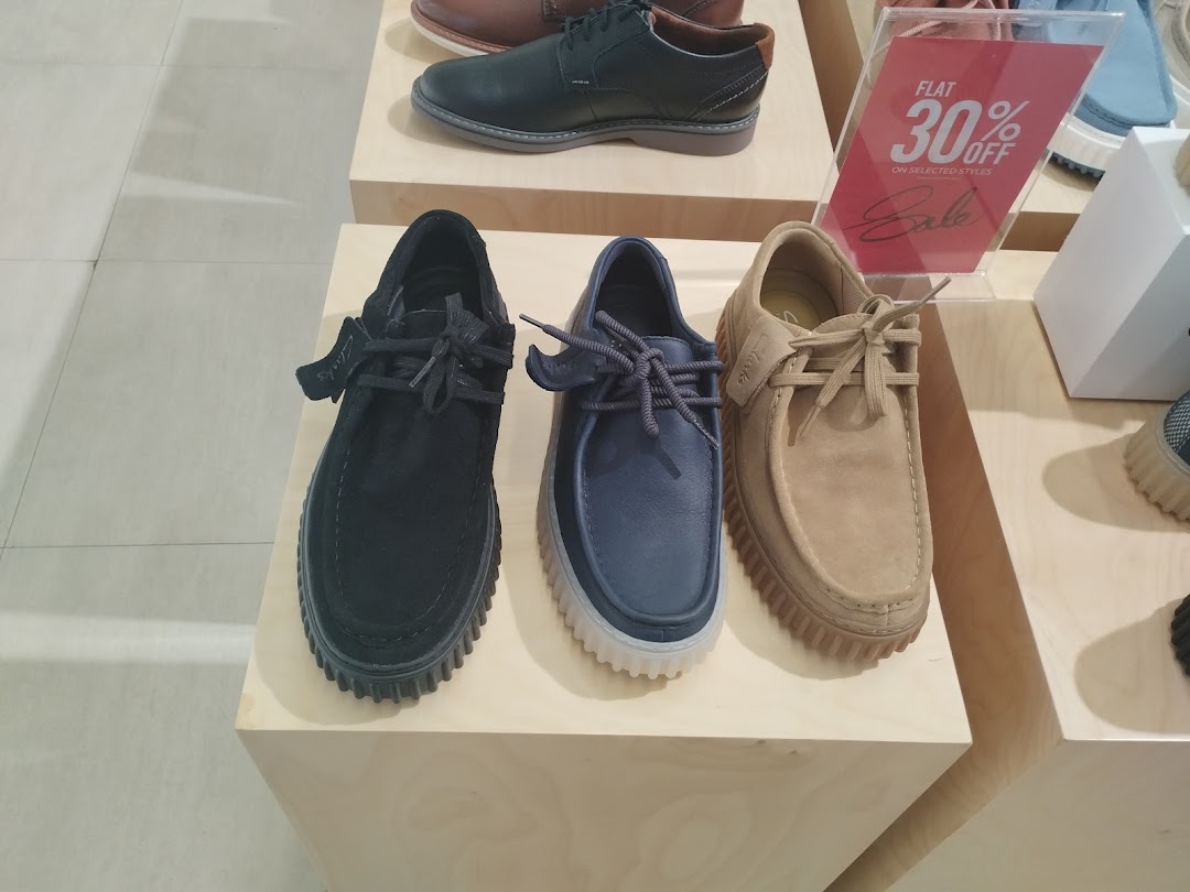 Three pairs of Clarks shoes displayed on wooden shelves with a sale sign.