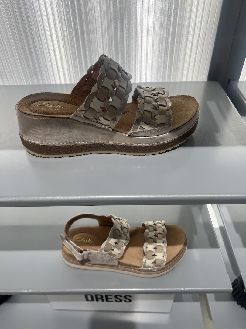 Two pairs of stylish Clarks sandals with woven straps displayed on shelves.