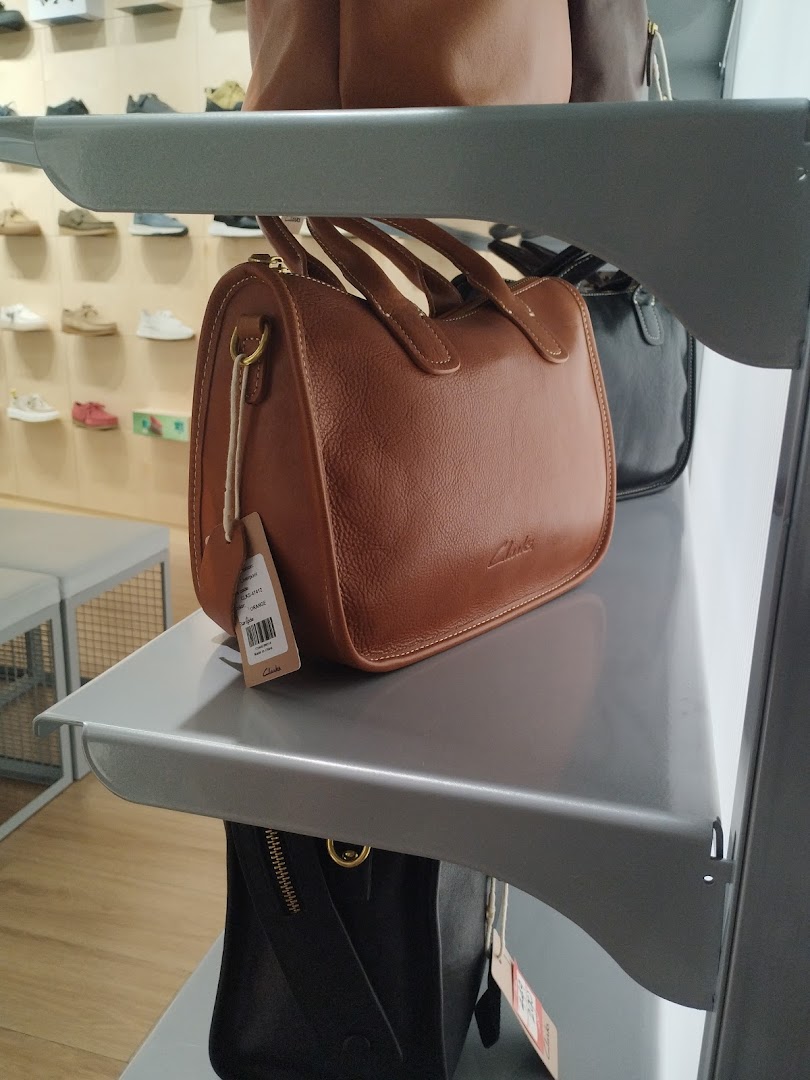 A brown leather handbag is displayed on a shelf in a retail store, with other bags and shoes visible.