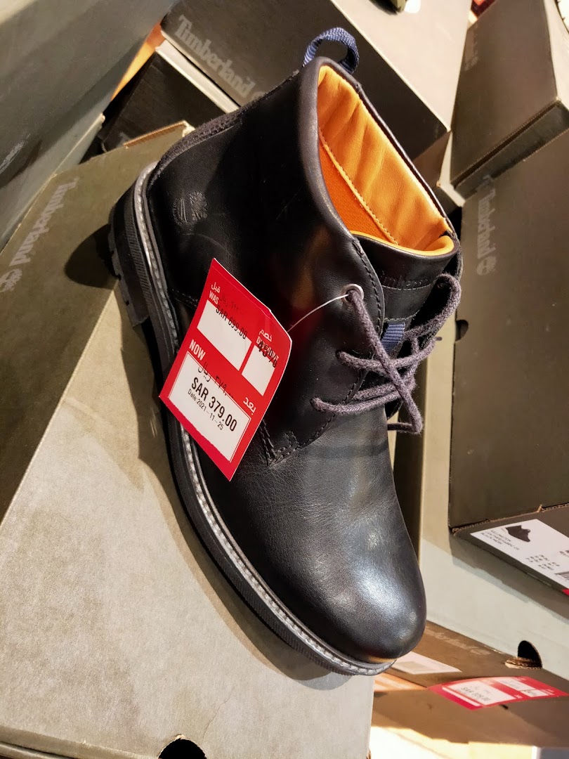 A black Timberland boot with a red sale tag is displayed on a box.