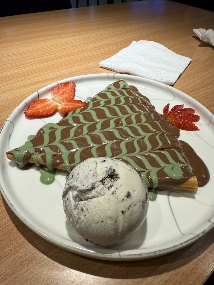 A delicious crepe topped with chocolate and pistachio sauce, served with strawberries and ice cream.