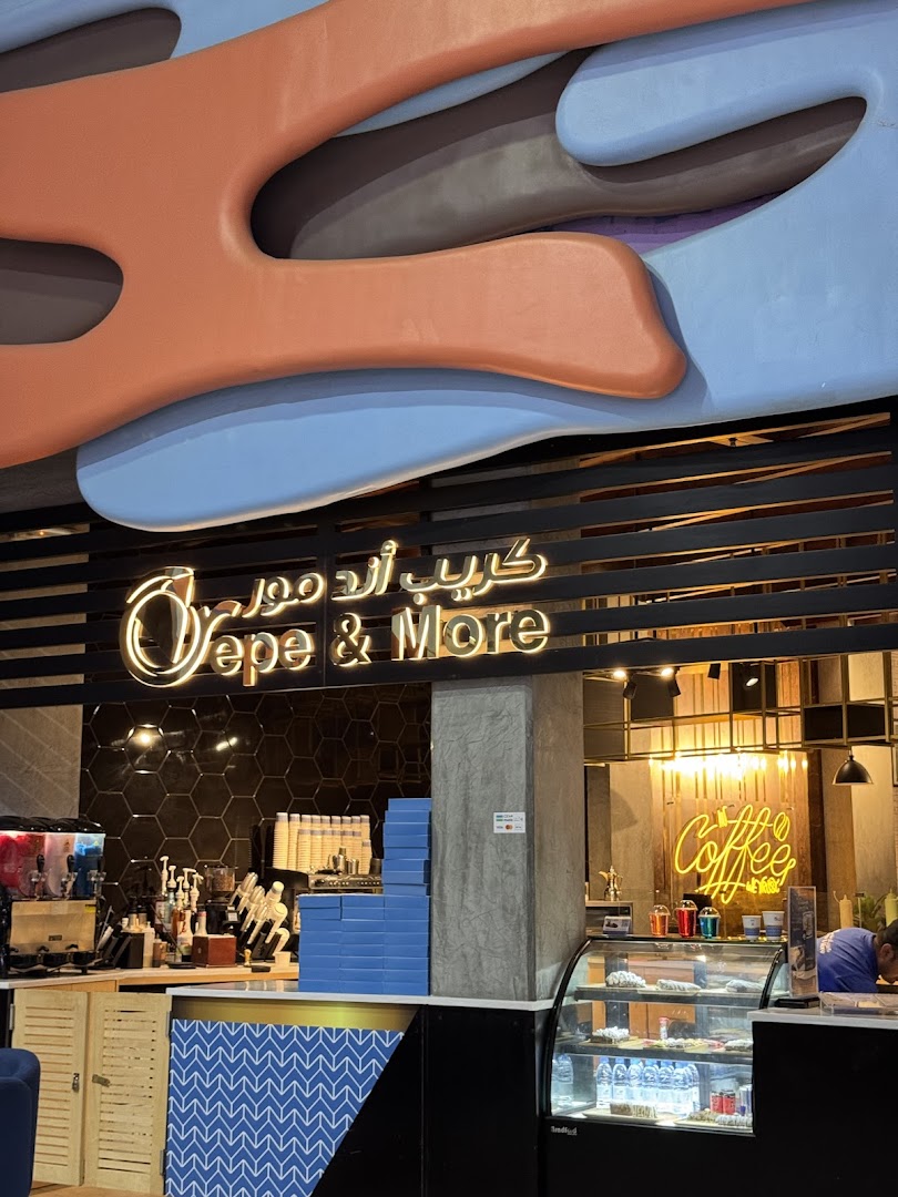 The entrance of Crepe & More, featuring a neon sign and a display of crepes and drinks.