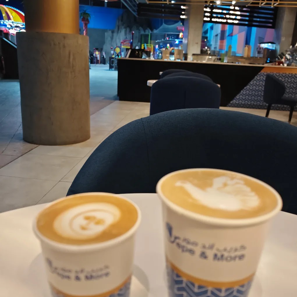Two cups of coffee with latte art sit on a table in front of a cafe counter.