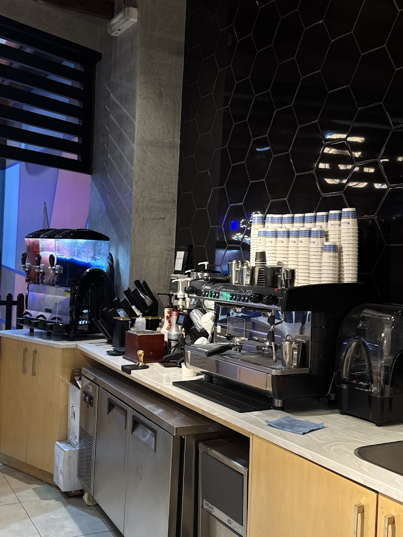 A coffee shop counter with espresso machines, cups, and a beverage dispenser.