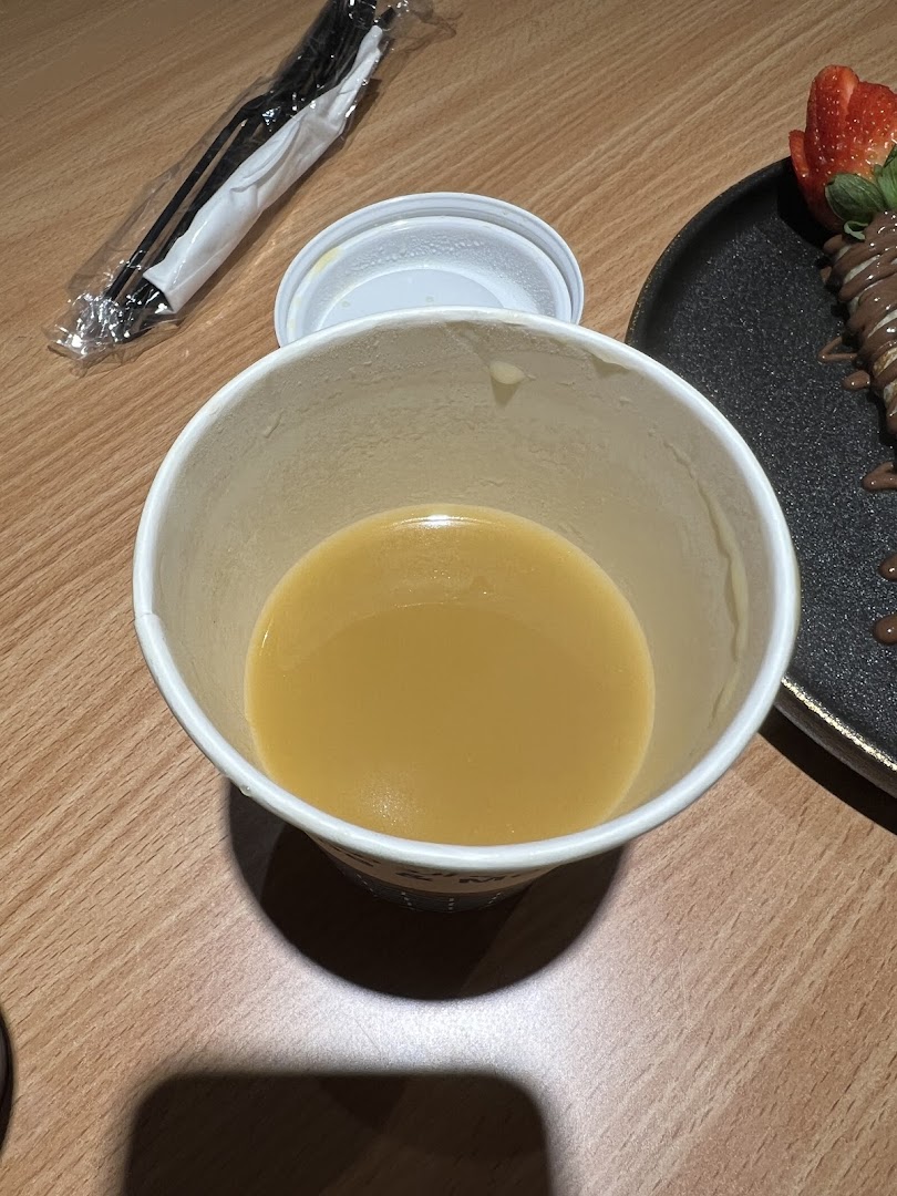 A close-up of a cup of beverage with a crepe and strawberries in the background.