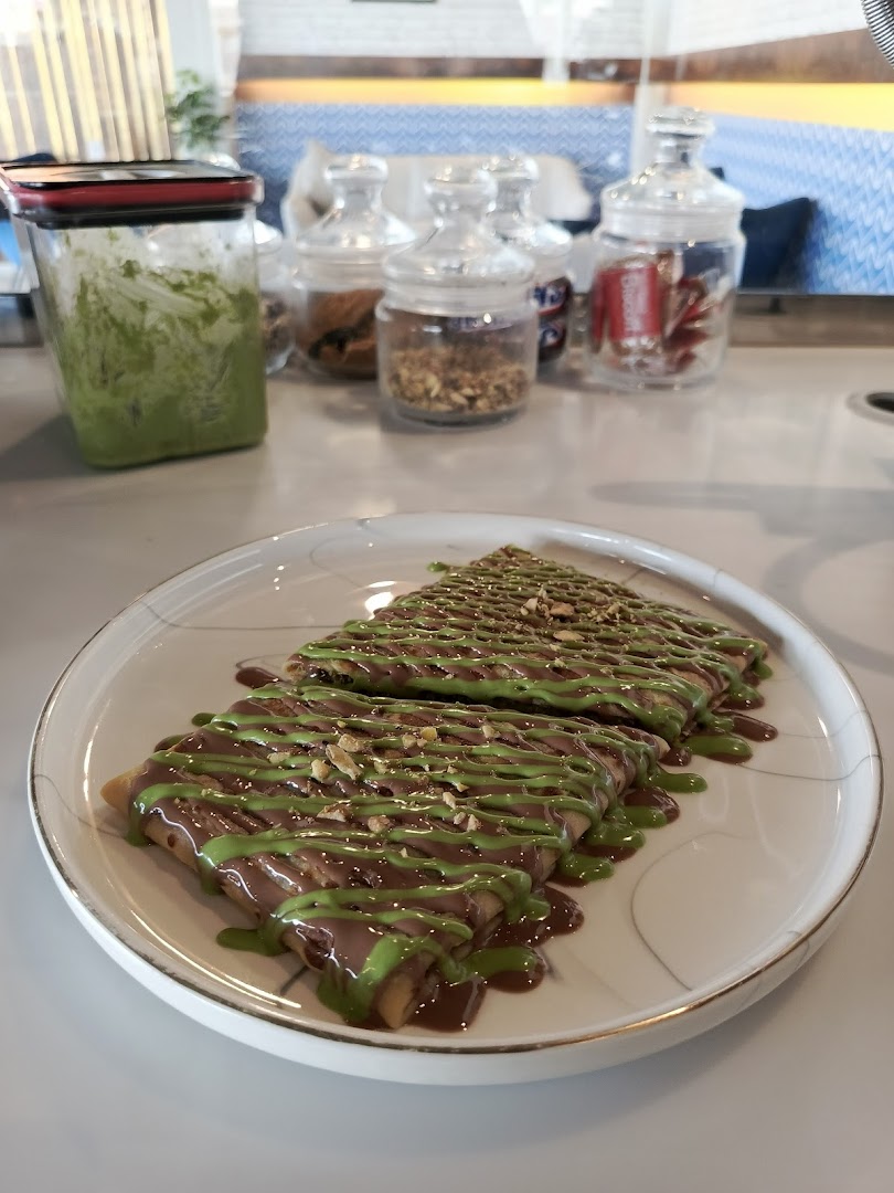 A plate of crepes drizzled with chocolate and green sauce, topped with nuts.