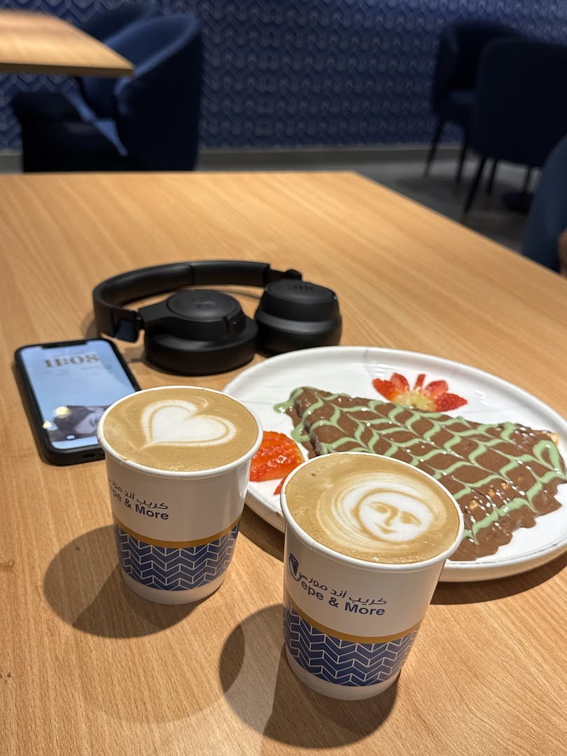 Two coffees and a crepe with chocolate and pistachio sauce on a wooden table.