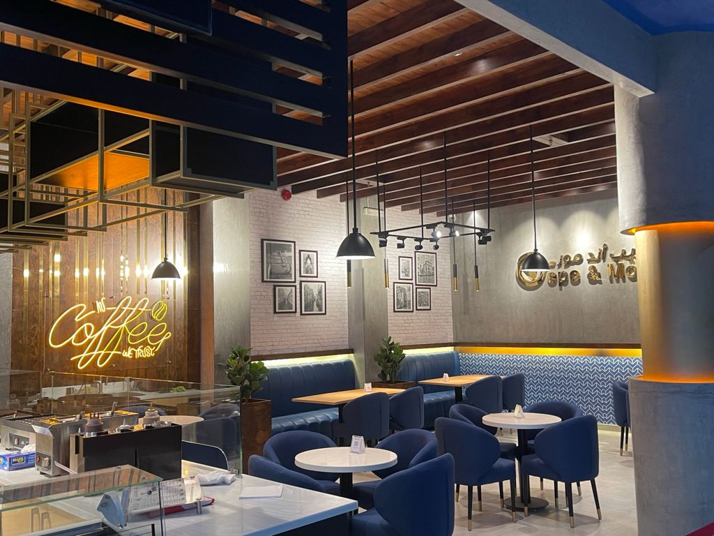 Interior of a modern cafe with blue seating, wooden ceiling, and neon coffee sign.