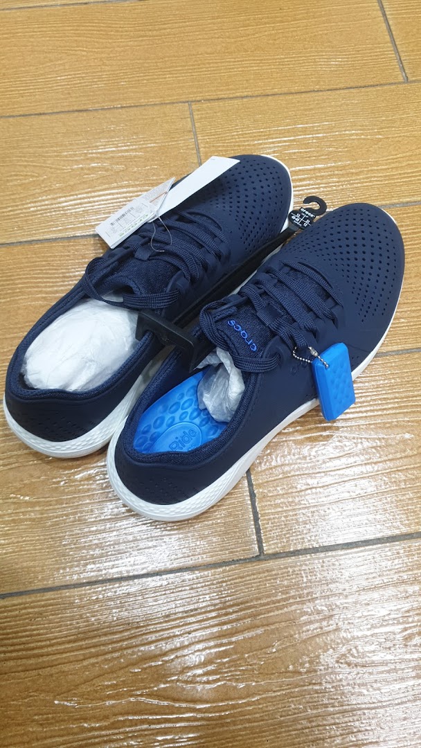 A pair of navy blue Crocs shoes with white soles and laces are displayed on a wooden floor.