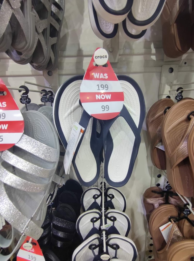 A display of Crocs sandals and flip-flops with sale tags indicating a price reduction.