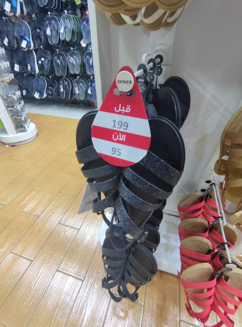 A display of sparkly black Crocs sandals with a sale tag showing a price reduction.