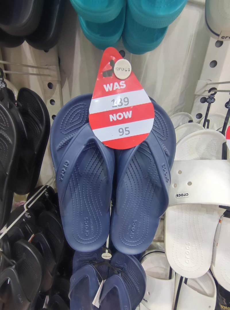A display of blue Crocs flip-flops with a sale tag showing a price reduction.