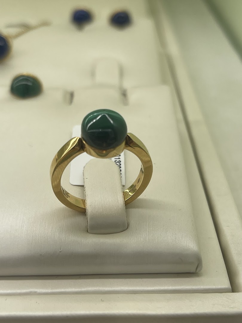 A close-up shot of a gold ring with a large green stone, displayed in a jewelry store.
