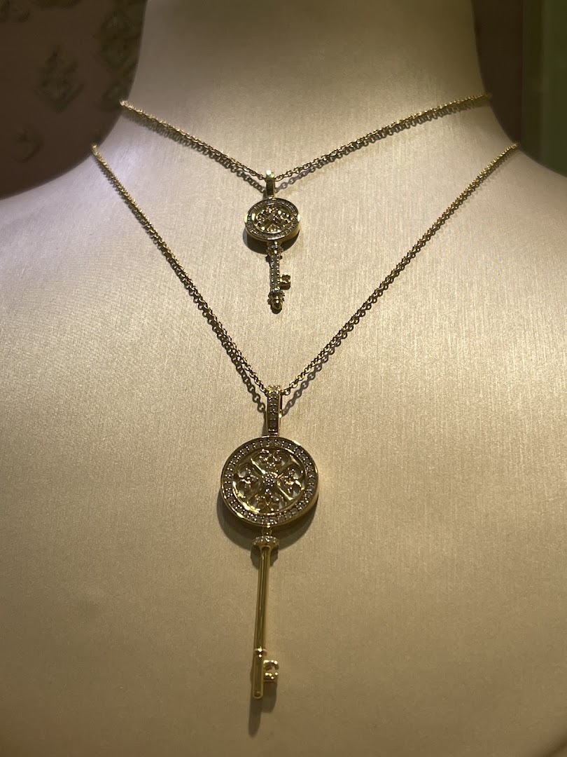 Two elegant gold necklaces with key-shaped pendants adorned with diamonds, displayed on mannequins.