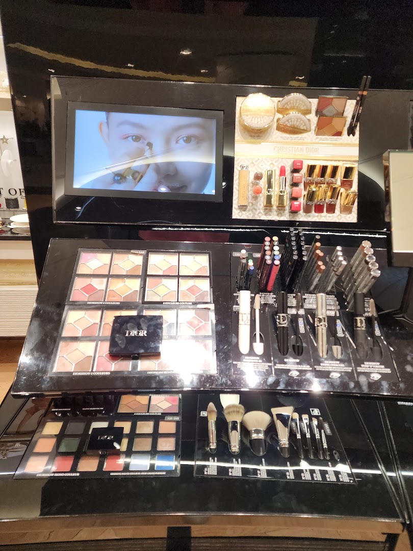 Dior makeup display featuring eyeshadow palettes, lipsticks, mascaras, and brushes.
