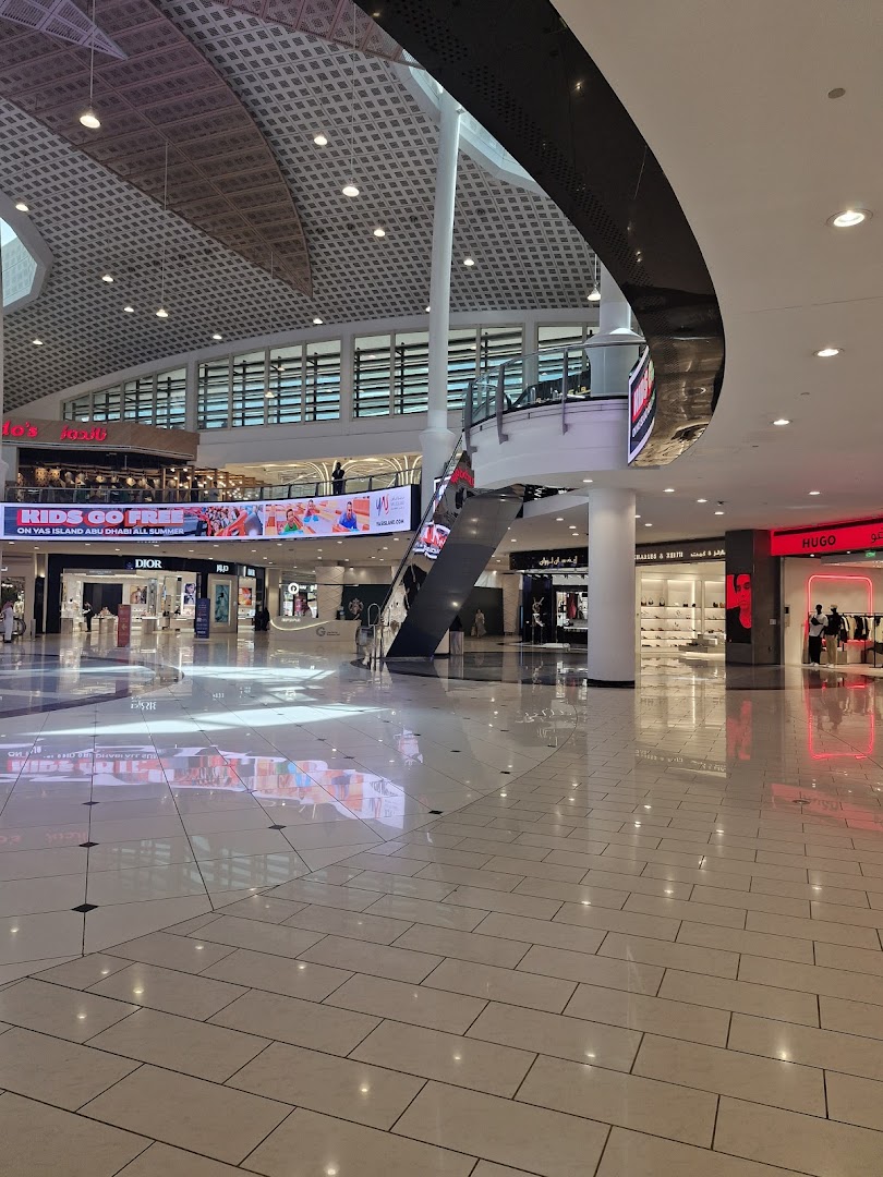 A wide view of a modern shopping mall interior with shops and escalators.