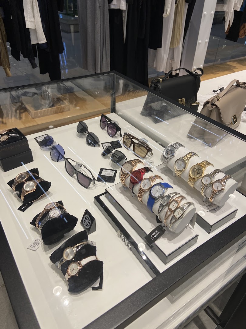 A display case filled with DKNY watches and sunglasses, with clothing visible in the background.