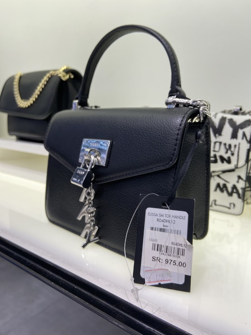 A black DKNY handbag with a silver lock and charm is displayed on a shelf.