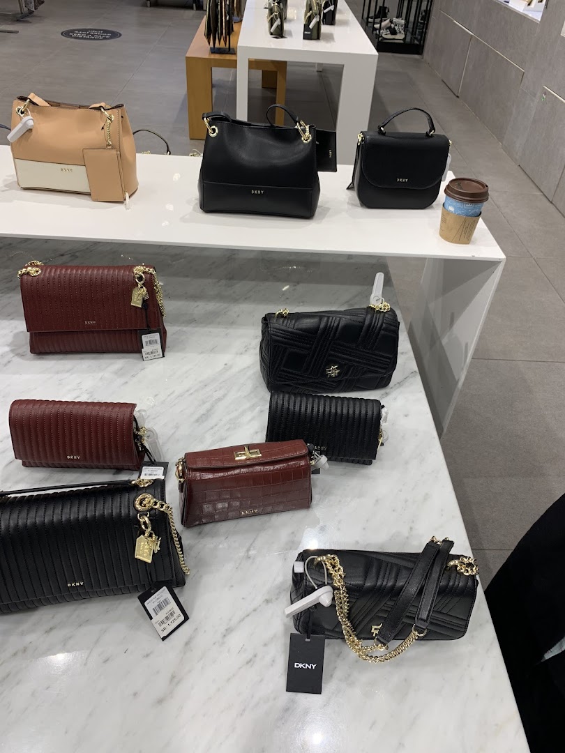 A display of various DKNY handbags in different colors and styles on white shelves.