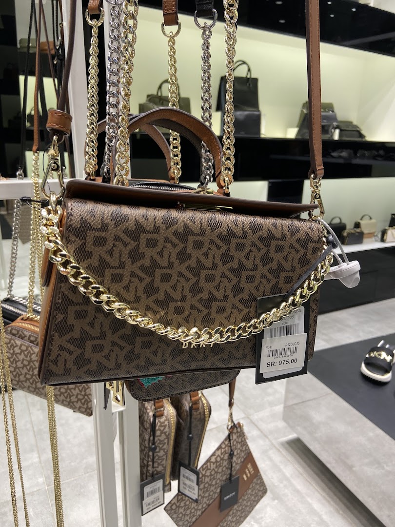 A close-up of a DKNY handbag with the signature logo pattern and a gold chain.