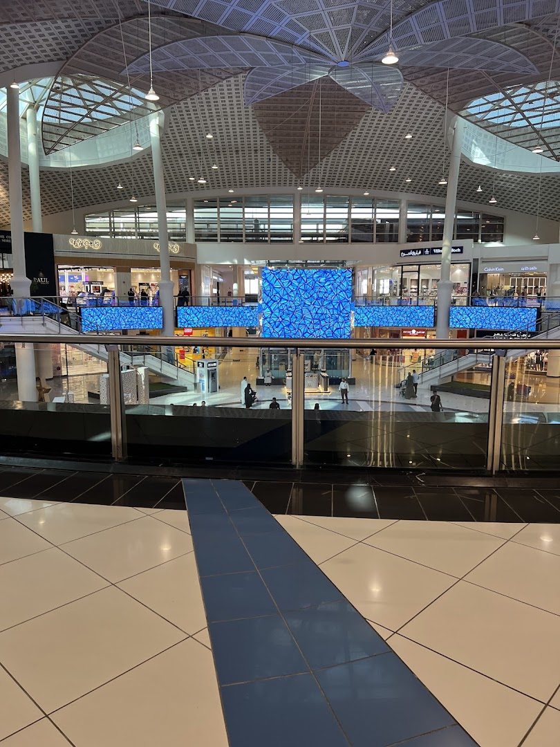Interior view of a modern shopping mall with shops and digital displays.