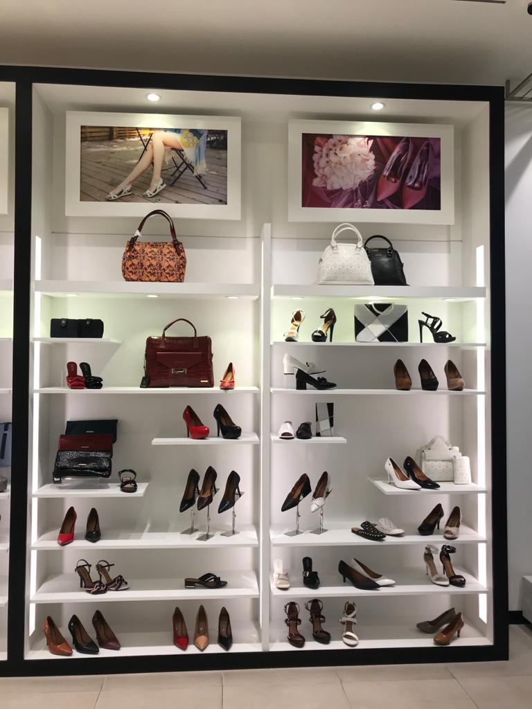 A well-lit display of women's shoes and handbags on shelves, with fashion imagery.