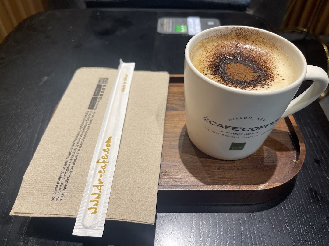 A cup of coffee with a straw and napkin on a wooden tray.