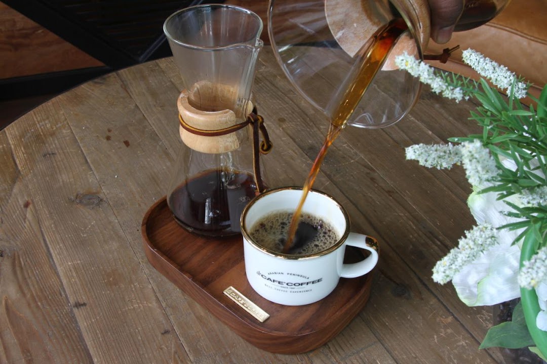 Freshly brewed coffee is poured from a Chemex into a branded mug on a wooden table.