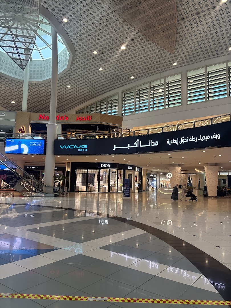 Interior view of a modern shopping mall with various retail stores and escalators.