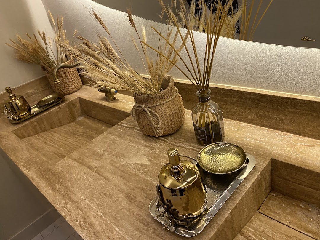 A luxurious bathroom vanity with a stone countertop, featuring gold soap dispensers and reed diffusers.
