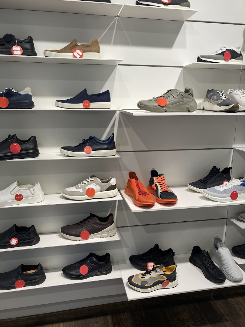 A display of various ECCO shoes on white shelves, many with red sale tags.