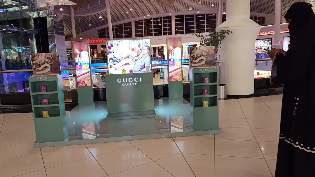 A Gucci Guilty fragrance display with digital screens and product shelves in a mall.