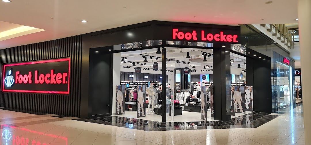 The exterior of a Foot Locker store with its prominent red logo and displays of clothing and mannequins.