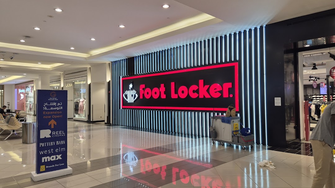 The Foot Locker store entrance in a mall with a large illuminated sign and vertical blue lights.