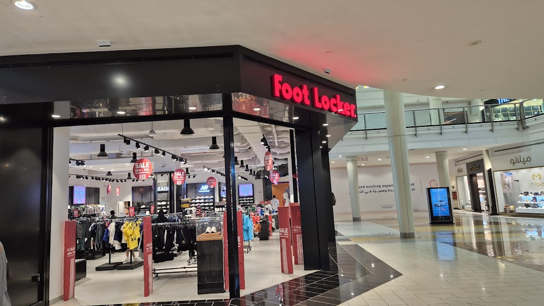 The entrance of a Foot Locker store showcasing apparel and footwear with sale signs.