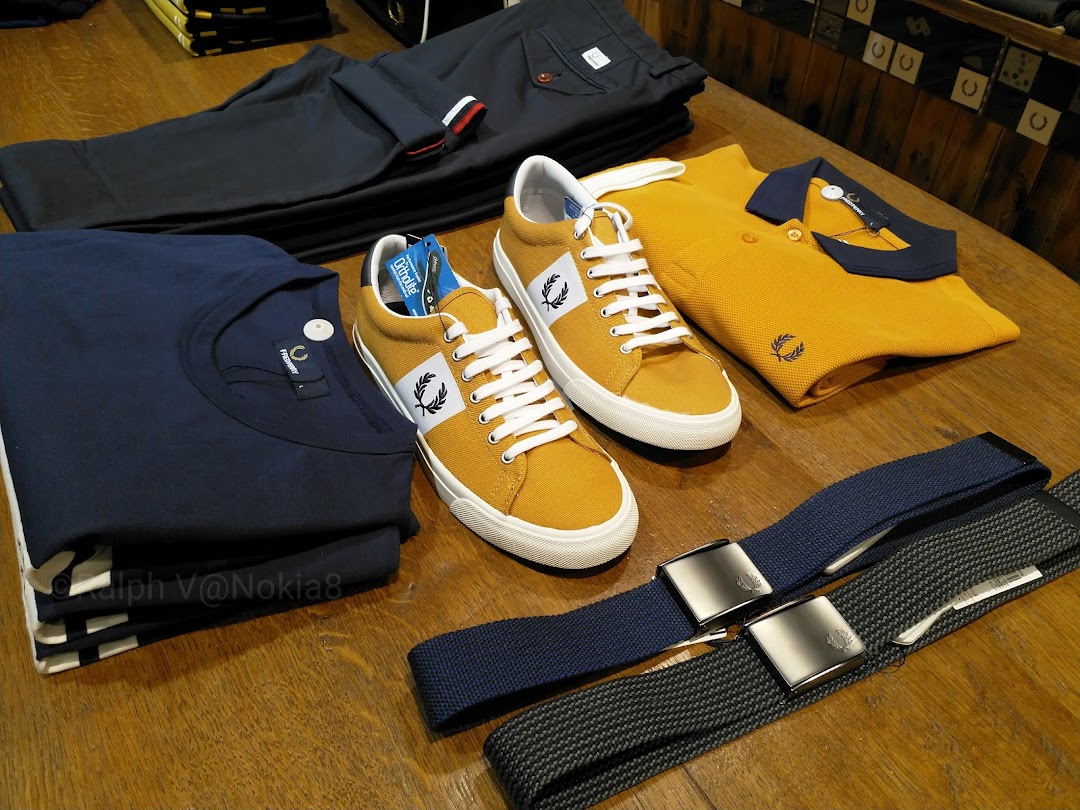 A collection of Fred Perry apparel and footwear, including shirts, trousers, shoes, and belts, neatly arranged on a wooden surface.
