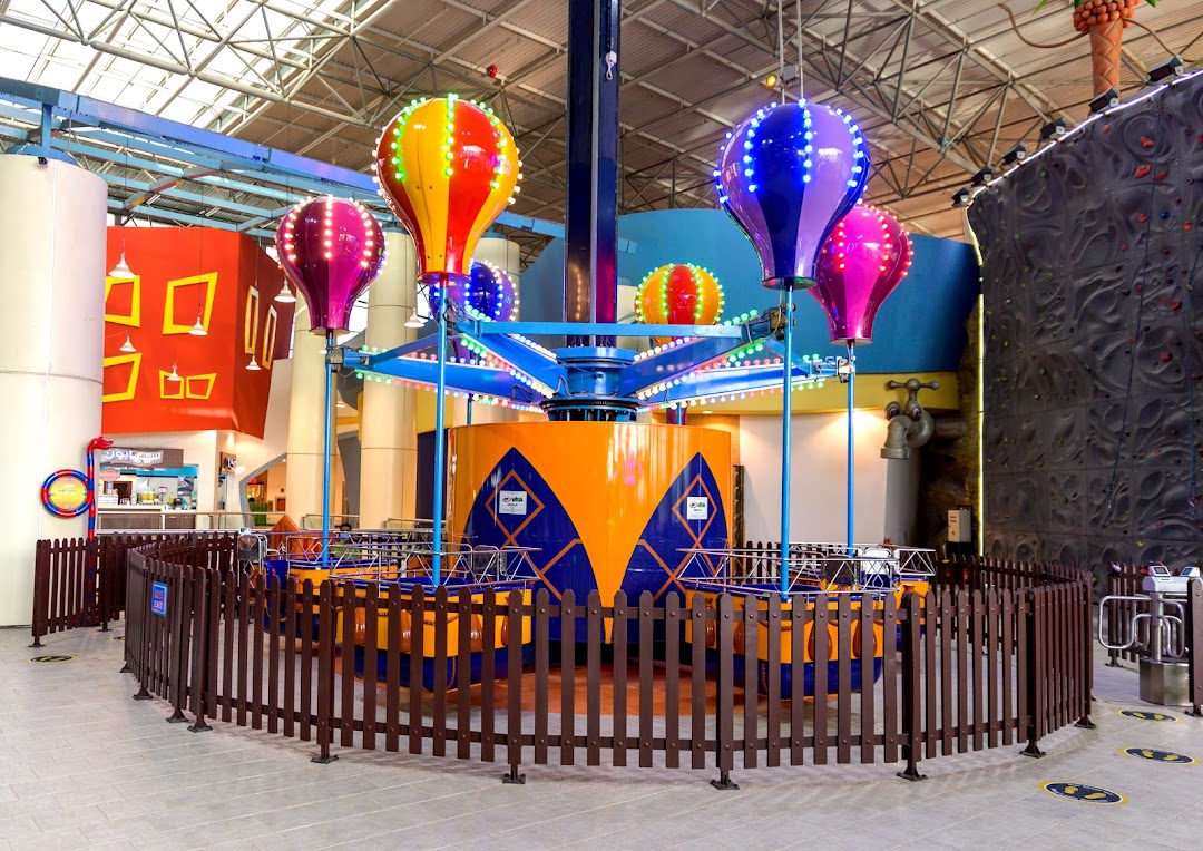 An indoor amusement park ride with colorful hot air balloon-themed cars and a climbing wall in the background.