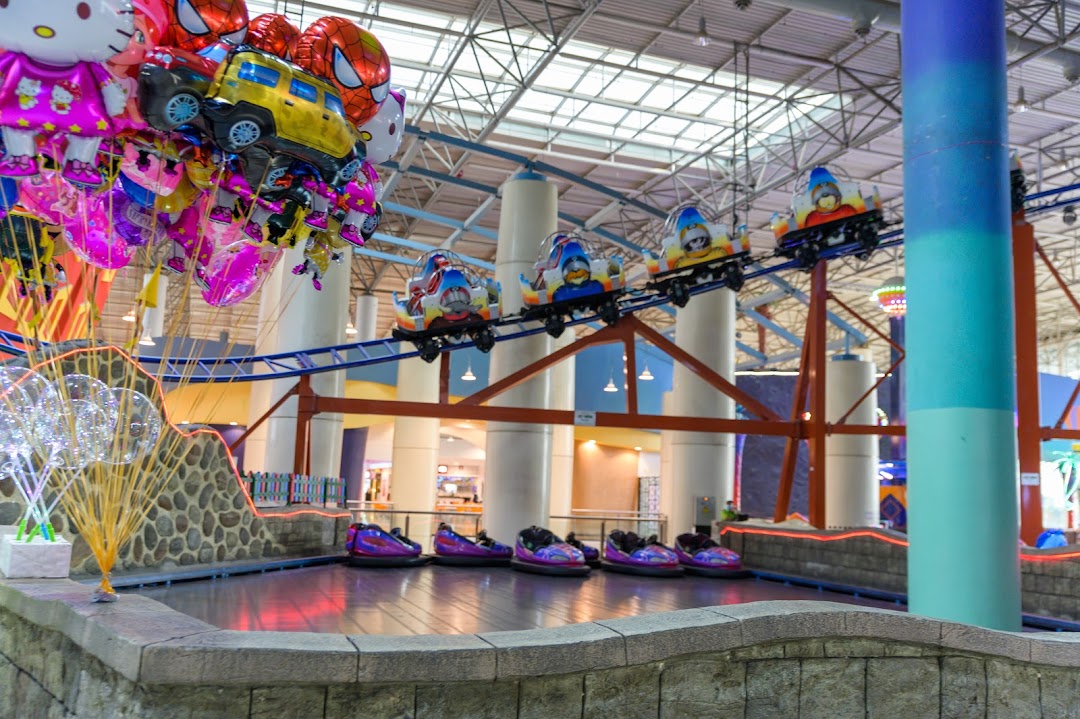 Indoor amusement park with bumper cars and a roller coaster ride, decorated with balloons.